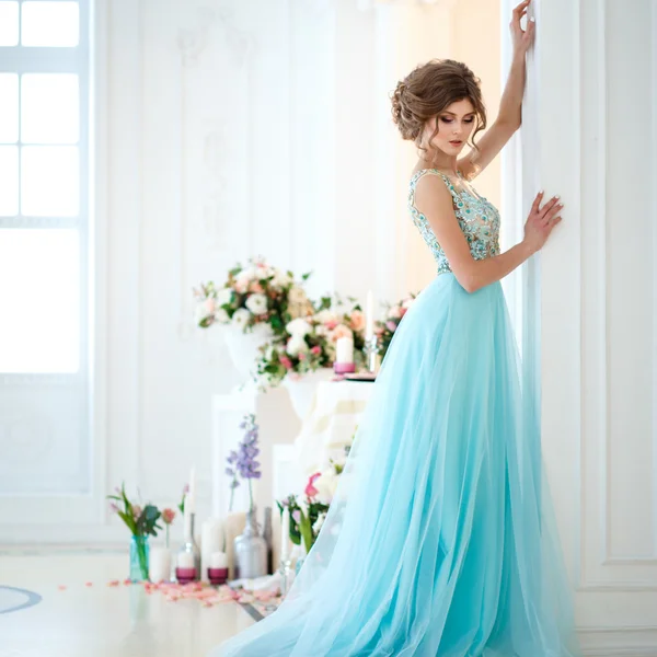 Mooie jonge dame in een luxe blauwe jurk in elegant interieur versierd met bloemen — Stockfoto