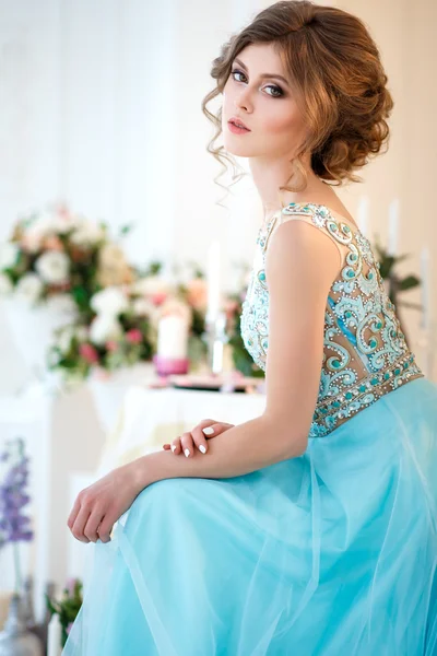 Hermosa joven en un vestido azul de lujo en un elegante interior decorado con flores — Foto de Stock