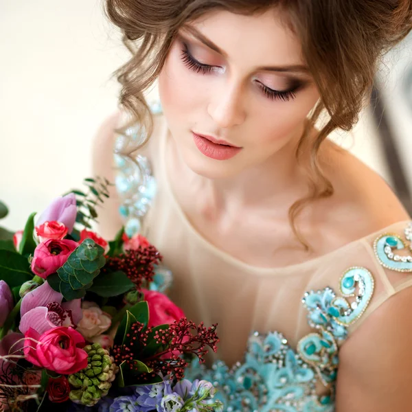 Hermosa joven en un vestido azul de lujo en un elegante interior con un ramo de flores — Foto de Stock