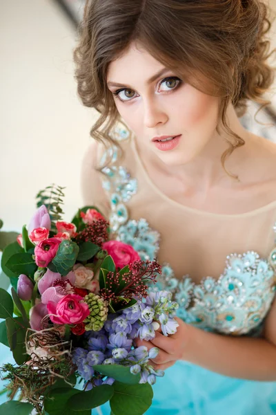 Menina bonita em um vestido azul de luxo em interior elegante com um buquê de flores — Fotografia de Stock