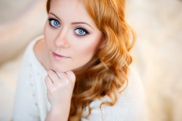 Junge schöne Frau in einem warmen Pullover in einem hellen Schlafzimmer an einem Morgen. Porträt aus nächster Nähe, blaue Augen und natürliches Make-up — Stockfoto