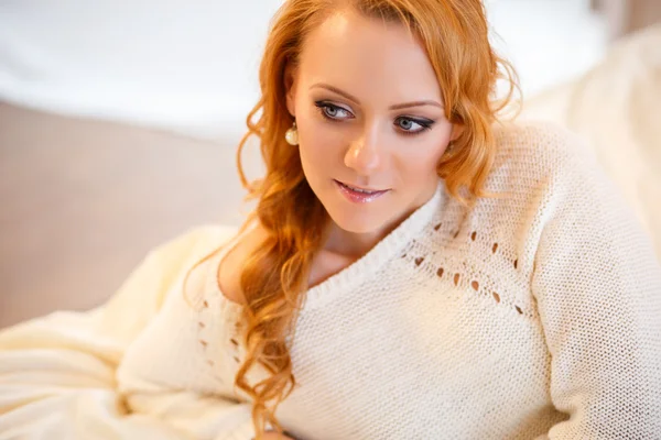 Young beautiful woman in a warm pullover in a light bedroom in a morning. Close up portrait, blue eyes and natural makeup — Stock Photo, Image