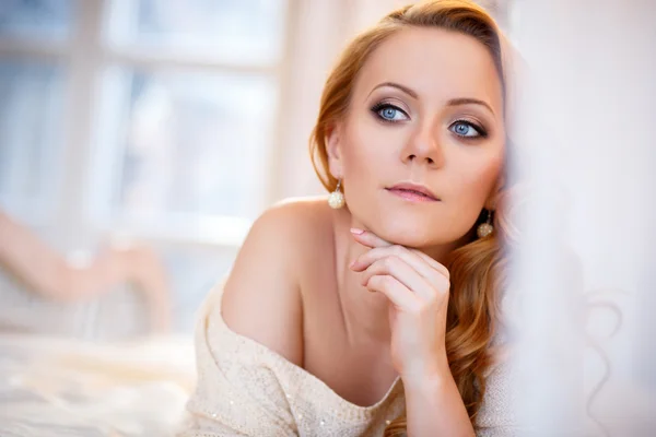 Joven hermosa mujer en un cálido jersey en un dormitorio luminoso en una mañana. Primer plano retrato, ojos azules y maquillaje natural —  Fotos de Stock