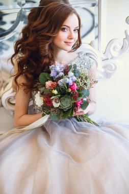 Ayna yakınında oturan çiçek bir buket ile zarif iç lüks bir elbise içinde güzel genç bayan