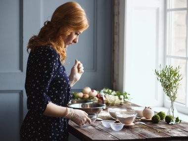 Young woman prepare bath bombs. Ingredients and floral decor on a wooden vintage table.