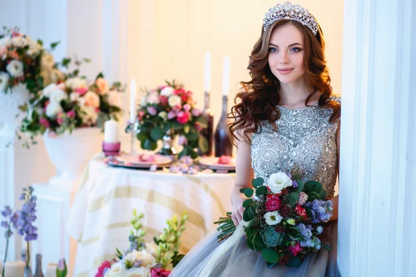 Beautiful young lady in a luxury dress in elegant interior with a bouquet of flowers