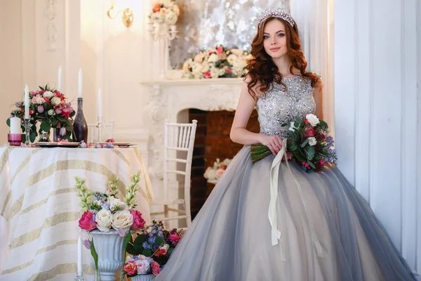 Hermosa joven en un vestido de lujo en un elegante interior con un ramo de flores —  Fotos de Stock