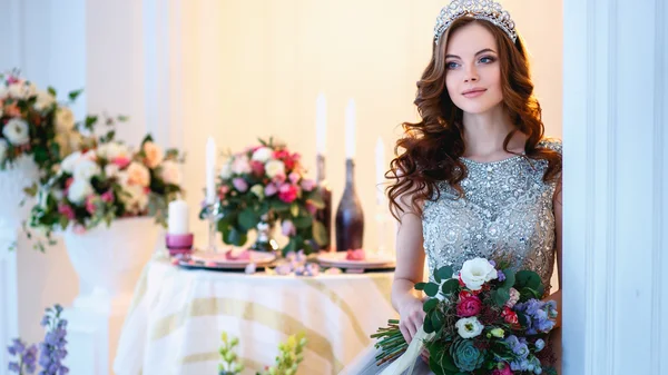 Schöne junge Dame in einem luxuriösen Kleid in elegantem Interieur mit einem Blumenstrauß — Stockfoto