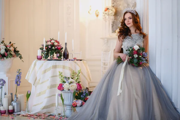 Schöne junge Dame in einem luxuriösen Kleid in elegantem Interieur mit einem Blumenstrauß — Stockfoto