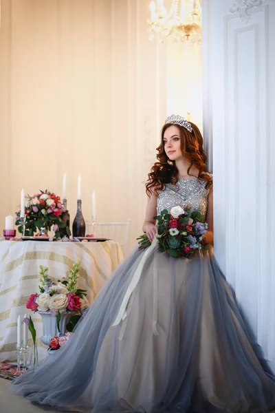 Hermosa joven en un vestido de lujo en un elegante interior con un ramo de flores — Foto de Stock