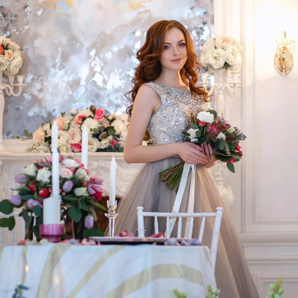 Hermosa joven en un vestido de lujo en un elegante interior con un ramo de flores —  Fotos de Stock