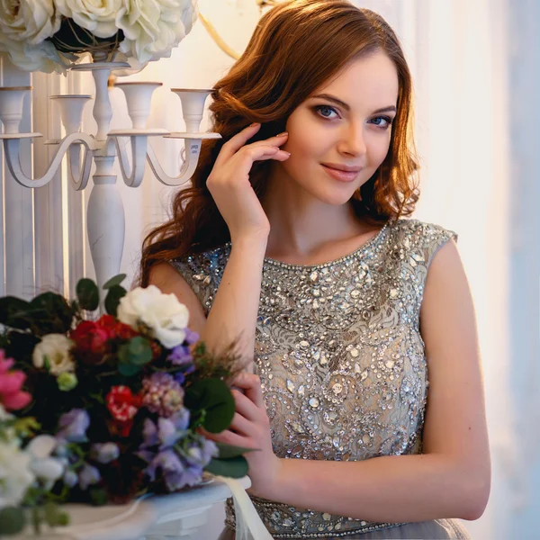 Hermosa joven en un vestido de lujo en un elegante interior con un ramo de flores — Foto de Stock