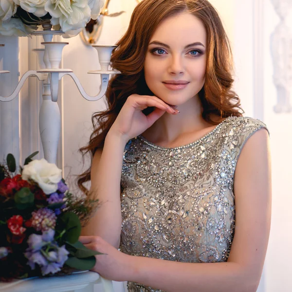 Piękna młoda dama w luksusowej sukni w eleganckim wnętrzu z bukietem kwiatów — Zdjęcie stockowe