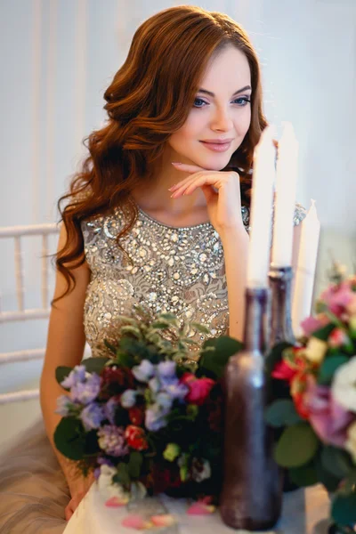 Piękna młoda dama w sukni luksus niebieski siedzący przy stole z bukietem kwiatów — Zdjęcie stockowe