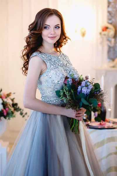 Piękna młoda dama w luksusowej sukni w eleganckim wnętrzu z bukietem kwiatów — Zdjęcie stockowe