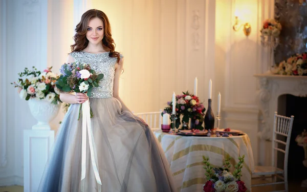 Menina bonita em um vestido de luxo em interior elegante com um buquê de flores — Fotografia de Stock