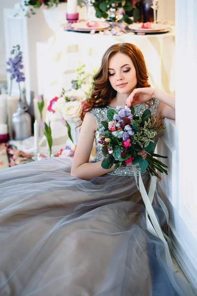 Hermosa joven en un vestido de lujo en un elegante interior con un ramo de flores — Foto de Stock