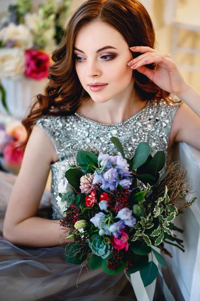 Schöne junge Dame in einem luxuriösen Kleid in elegantem Interieur mit einem Blumenstrauß — Stockfoto