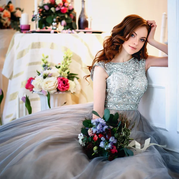 Schöne junge Dame in einem luxuriösen Kleid in elegantem Interieur mit einem Blumenstrauß — Stockfoto