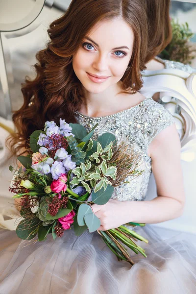 Schöne junge Dame in einem Luxuskleid in elegantem Interieur mit einem Blumenstrauß, der neben dem Spiegel sitzt — Stockfoto