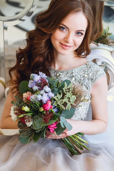 Hermosa joven en un vestido de lujo en un elegante interior con un ramo de flores sentado cerca del espejo —  Fotos de Stock