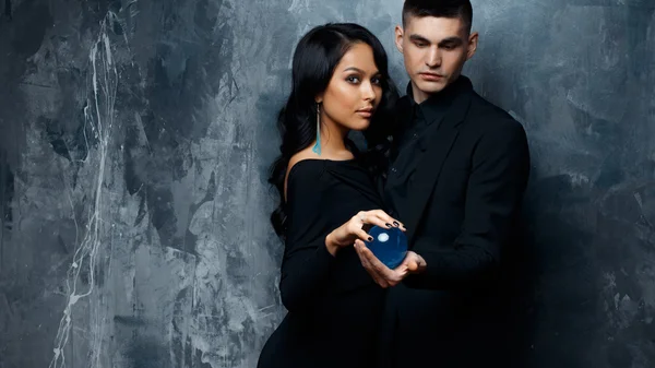 Homem jovem mágico e sua mulher assistente em uma roupa preta segurar uma esfera mágica — Fotografia de Stock