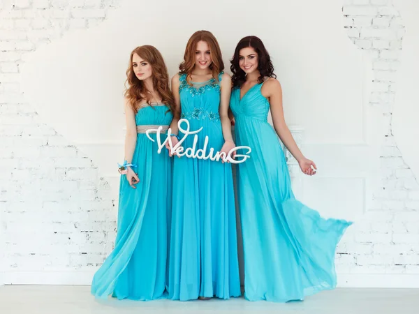 Three beautiful bridesmaids in similar blue dresses with perfect make up and hair style in a light loft space — Stock Photo, Image