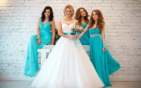 Bride and three bridesmaids in similar blue dresses with perfect make up and hair style in a light loft space — Stock Photo, Image