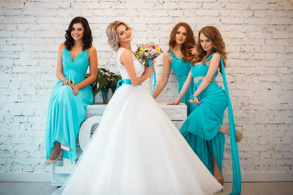 Bride and three bridesmaids in similar blue dresses with perfect make up and hair style in a light loft space — Stock Photo, Image
