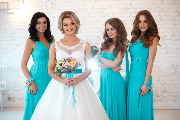 Bride and three bridesmaids in similar blue dresses with perfect make up and hair style in a light loft space — Stock Photo, Image