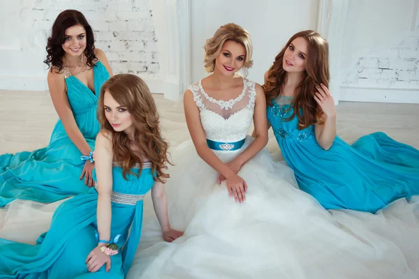 Bride and three bridesmaids in similar blue dresses with perfect make up and hair style in a light loft space — Stock Photo, Image