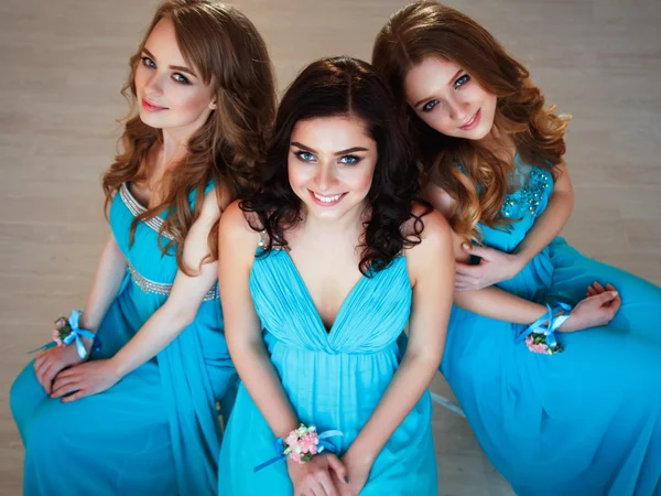 Three beautiful bridesmaids in similar blue dresses with perfect make up and hair style in a light loft space — Stock Photo, Image