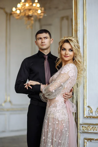 Gorgeous young woman with perfect makeup and hair style in luxury dress with a man in black clothes in interior