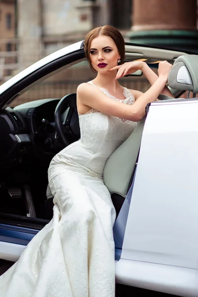 Noiva linda com maquiagem de moda e penteado em um vestido de noiva de luxo em um carro cabriolet branco — Fotografia de Stock