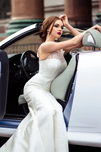 Noiva linda com maquiagem de moda e penteado em um vestido de noiva de luxo em um carro cabriolet branco — Fotografia de Stock