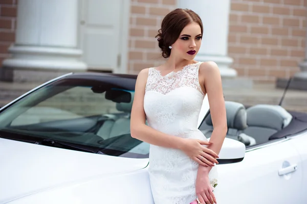 Noiva linda com maquiagem de moda e penteado em um vestido de casamento de luxo perto do carro cabriolet branco — Fotografia de Stock