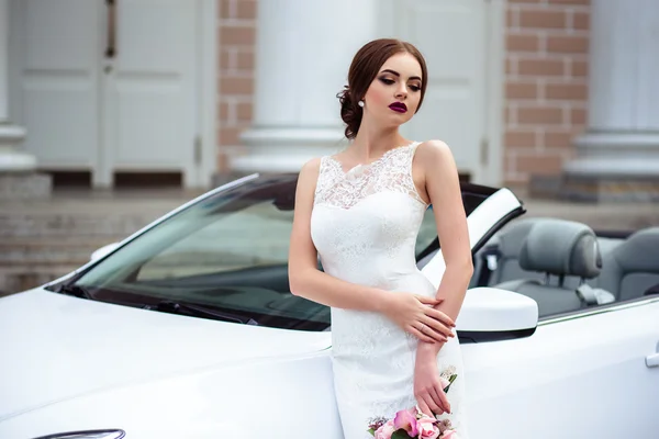 Noiva linda com maquiagem de moda e penteado em um vestido de casamento de luxo perto do carro cabriolet branco — Fotografia de Stock