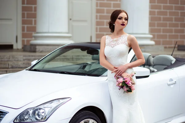 Noiva linda com maquiagem de moda e penteado em um vestido de casamento de luxo perto do carro cabriolet branco — Fotografia de Stock