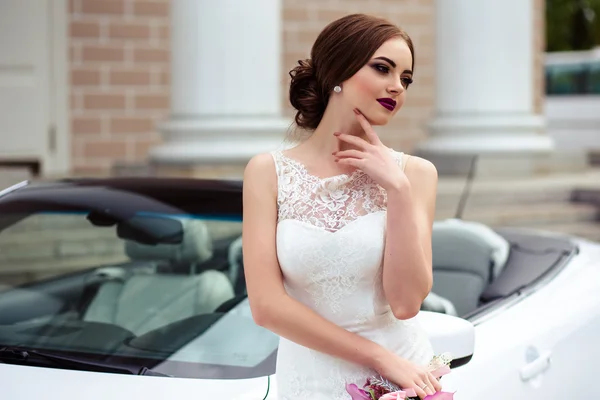 Noiva linda com maquiagem de moda e penteado em um vestido de casamento de luxo perto do carro cabriolet branco — Fotografia de Stock