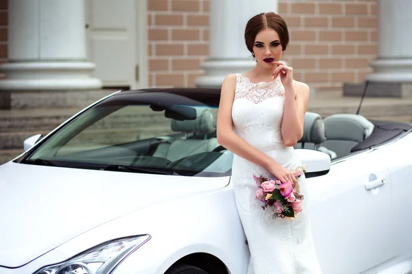 Noiva linda com maquiagem de moda e penteado em um vestido de casamento de luxo perto do carro cabriolet branco — Fotografia de Stock