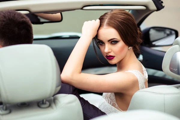 Pengantin cantik dengan riasan busana dan gaya rambut dalam gaun pengantin mewah dalam mobil berwarna putih berwarna ungu — Stok Foto