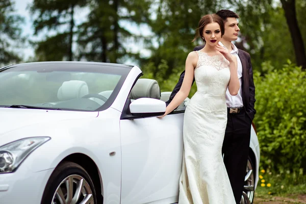 Gyönyörű mennyasszonyi divat smink és frizura, egy luxus esküvői ruha, a vőlegény jóképű közelében fehér cabriolet-autó — Stock Fotó