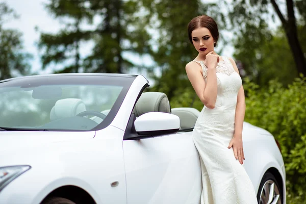 Noiva linda com maquiagem de moda e penteado em um vestido de casamento de luxo perto do carro cabriolet branco — Fotografia de Stock