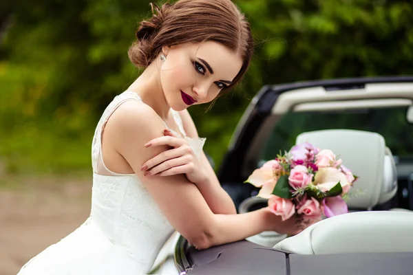 Wspaniałą narzeczoną z mody makijaż i fryzurę w sukni ślubnej luksusowych w pobliżu cabriolet biały samochód — Zdjęcie stockowe