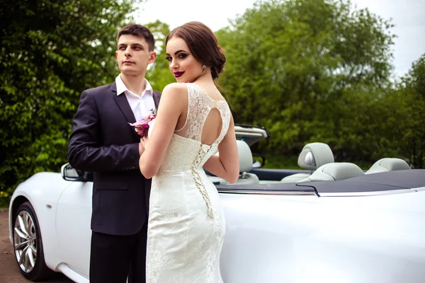 Gyönyörű mennyasszonyi divat smink és frizura, egy luxus esküvői ruha, a vőlegény jóképű közelében fehér cabriolet-autó — Stock Fotó
