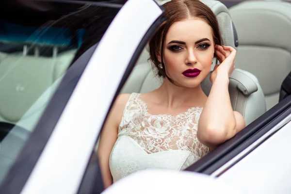 Pengantin cantik dengan riasan busana dan gaya rambut dalam gaun pengantin mewah dalam mobil berwarna putih berwarna ungu — Stok Foto