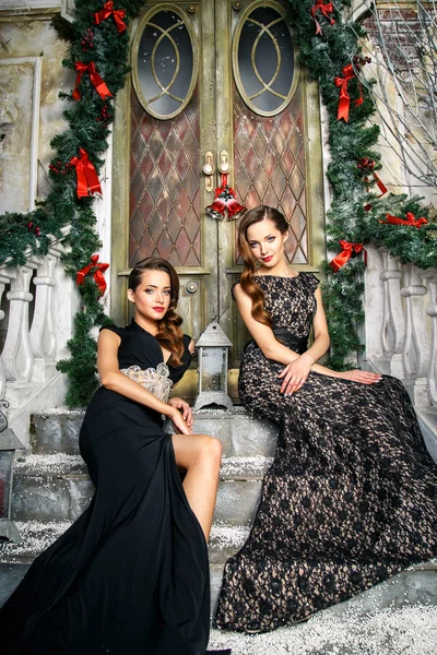 Portrait of beautiful twins young women in gorgeous evening dresses over christmas background — Stock Photo, Image