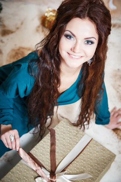 Beautiful young woman in evening dress holding present over Christmas background. — Stock Photo, Image