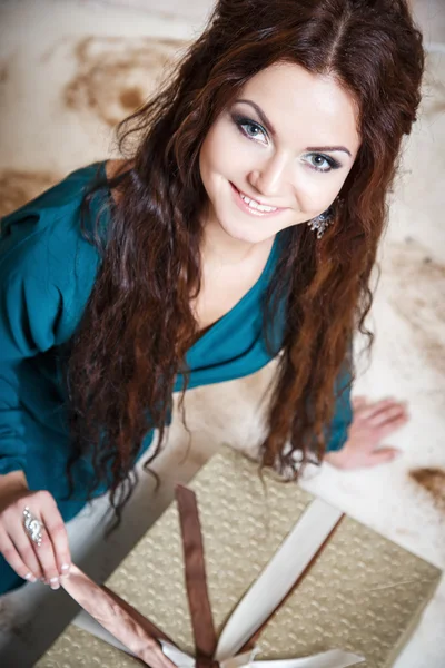 Schöne junge Frau im Abendkleid hält Geschenk über Weihnachten Hintergrund. — Stockfoto