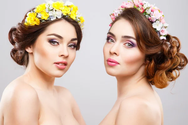 Retrato de hermosas gemelas mujeres jóvenes con maquillaje perfecto y peinado con flores en el pelo — Foto de Stock